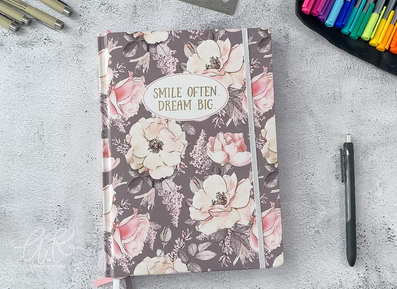 gray and pink hard cover floral notebook on table with pens