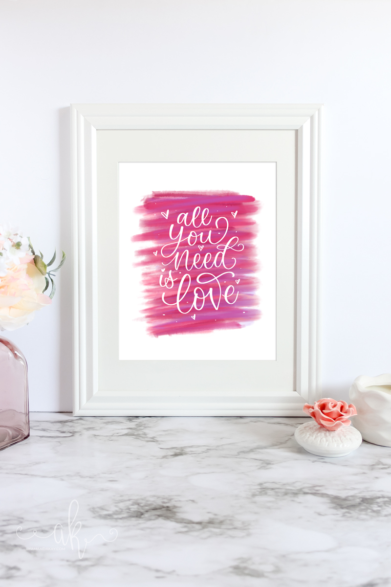 Digital "All you need is Love" artwork inside a frame on marble table with candle and flowers